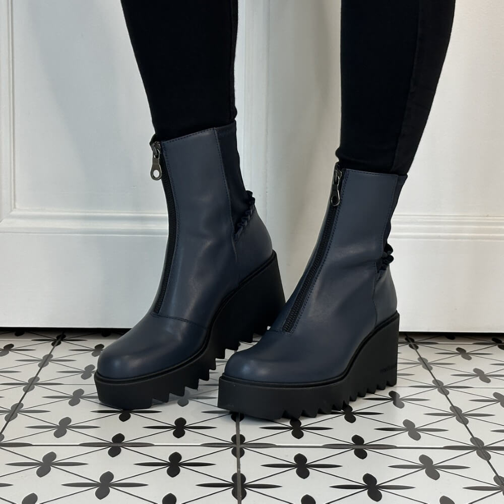 A pair of Marco Moreo dark navy blue leather ankle boots with chunky black platform wedge soles and front zippers, shown on a person wearing black leggings.