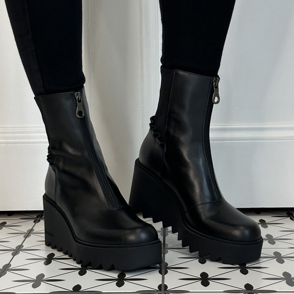 Marco Moreo Black platform ankle boots with front zippers, worn with black leggings on a black and white patterned tile floor in front of a white wall.