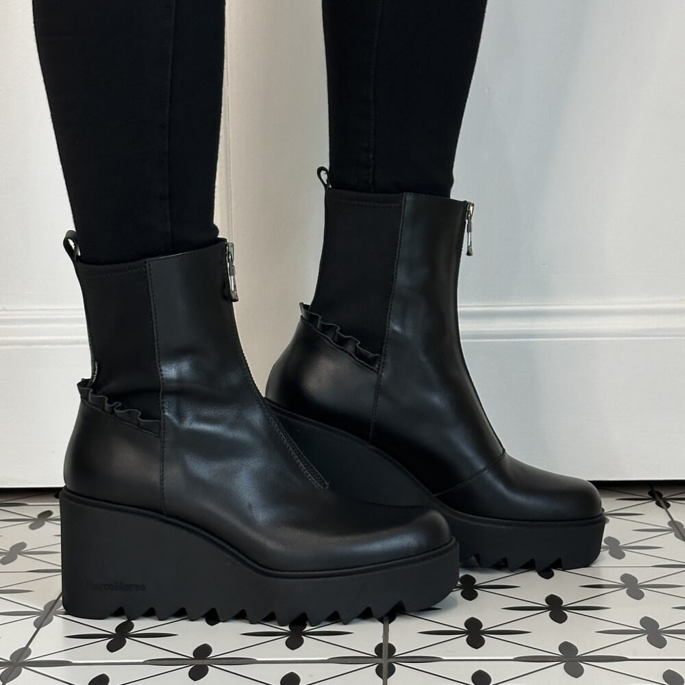 Marco Moreo Black platform ankle boots with front zippers, worn with black leggings on a black and white patterned tile floor in front of a white wall.
