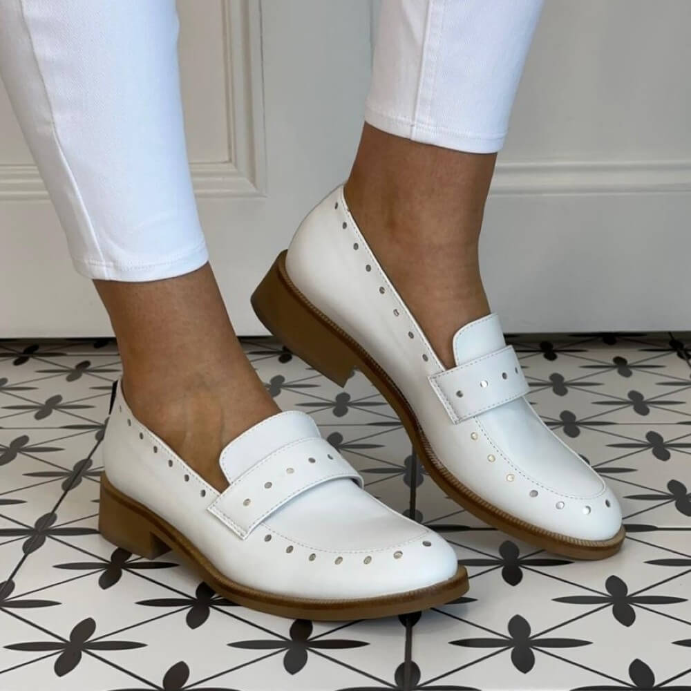 Marco Moreo White loafers worn with white pants on a patterned floor.