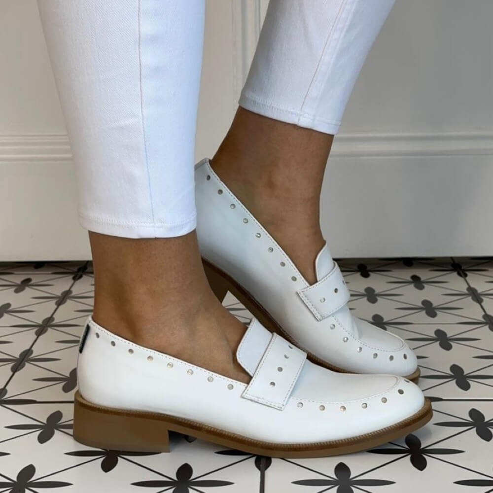 Marco Moreo White loafers worn with white pants on a patterned floor.