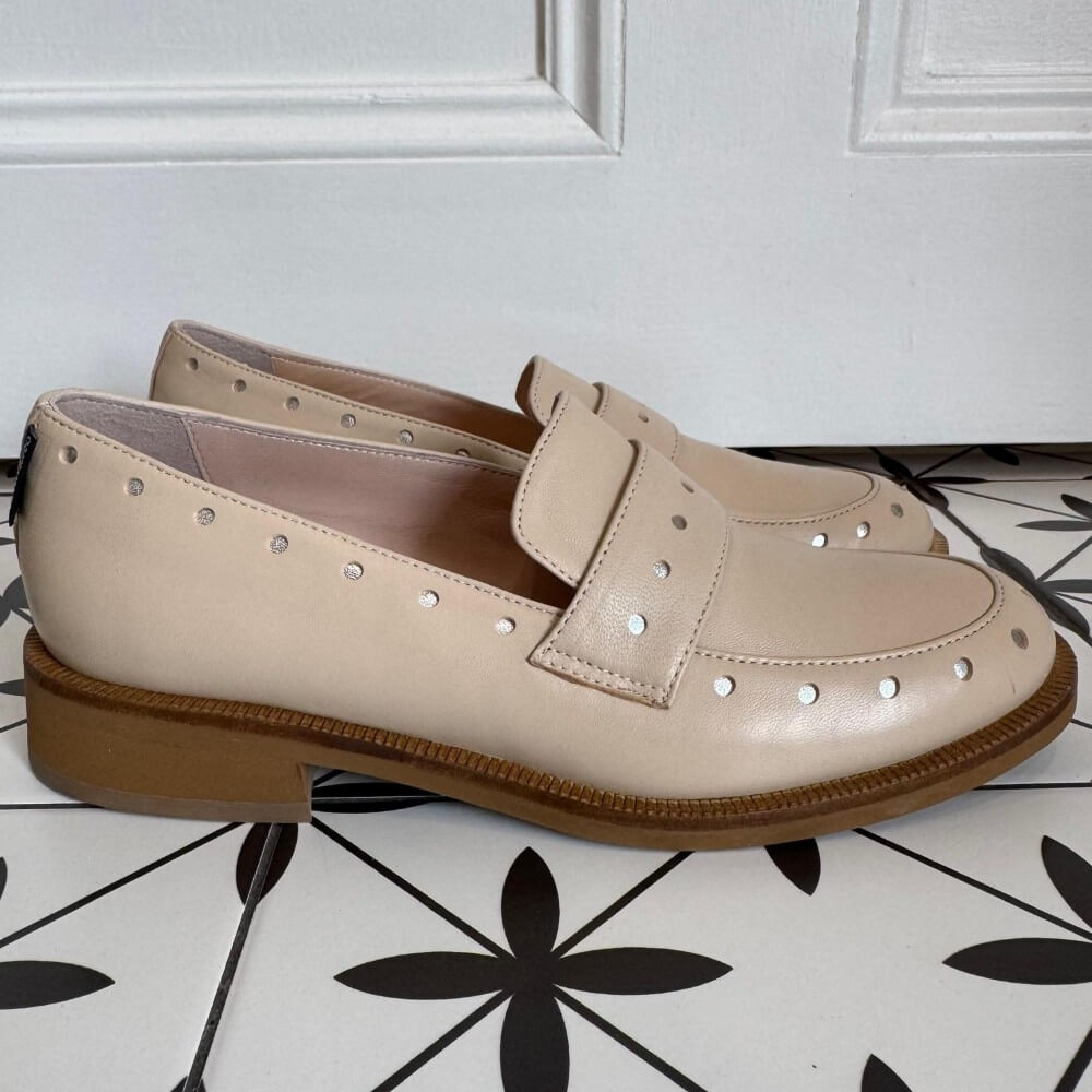 Pair of Marco Moreo beige loafers with brown soles on a white and black patterned floor. Maura X705