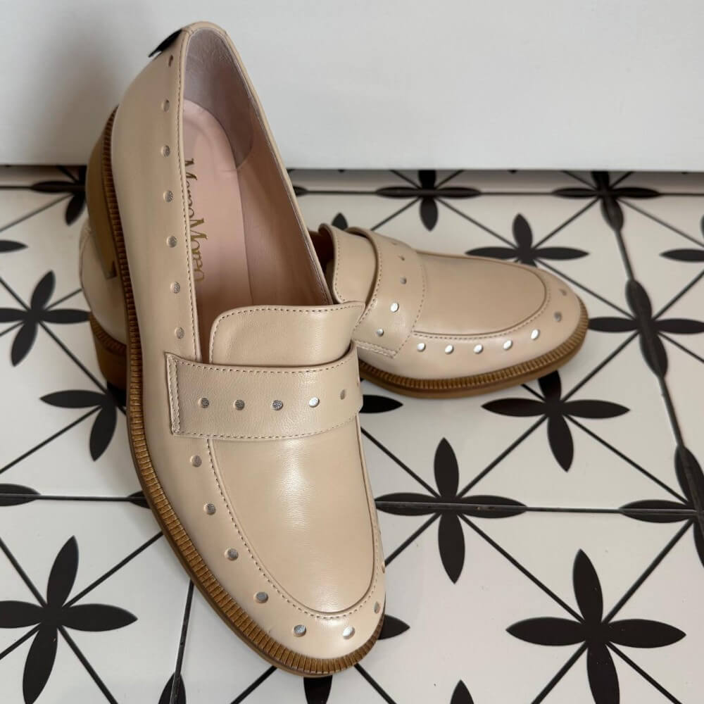 Pair of Marco Moreo beige loafers with brown soles on a white and black patterned floor. Maura X705