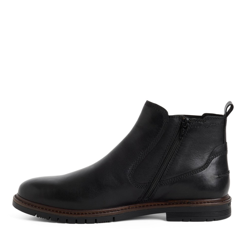 A Marco Tozzi Gents black leather Chelsea ankle boot with a side zipper, elastic side gore, and a brown welt sole, shown in profile against a white background.