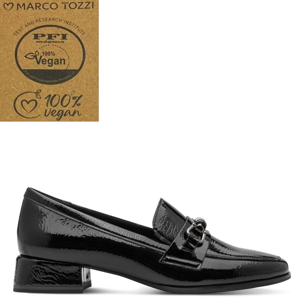 A Marco Tozzi black patent Vegan loafer by Marco Tozzi, featuring a low block heel and a decorative buckle strap across the vamp. The shoe is displayed on a clean white background with a brown cardboard certification badge in the top-left corner.
