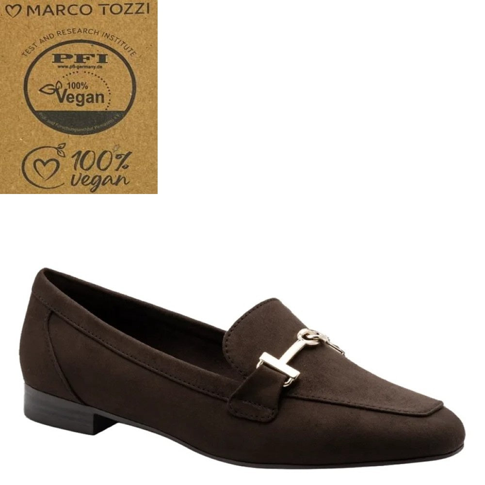 A dark brown Marco Tozzi vegan suede loafer with a small silver-tone horse bit detail on the strap, shown against a plain white background. In the top-left corner, there is a brown cardboard badge featuring the Marco Tozzi brand name and a PFI 100% Vegan certification logo.