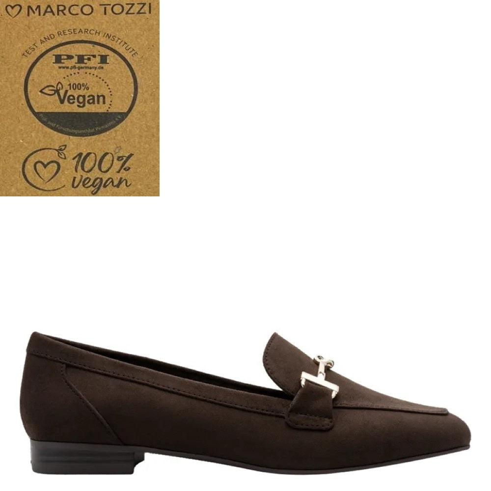 A dark brown Marco Tozzi vegan suede loafer with a small silver-tone horse bit detail on the strap, shown against a plain white background. In the top-left corner, there is a brown cardboard badge featuring the Marco Tozzi brand name and a PFI 100% Vegan certification logo.