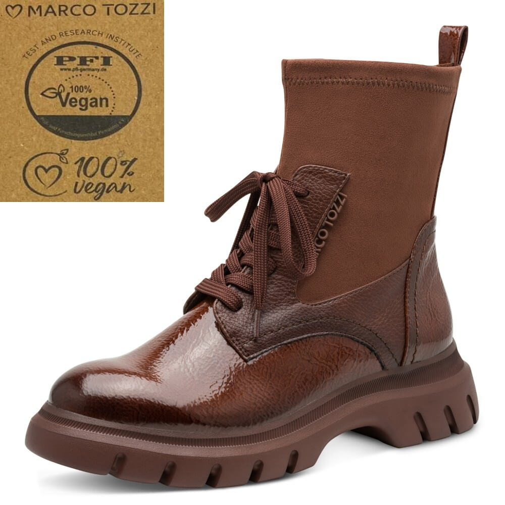 A Marco Tozzi brown ankle boot with a glossy patent leather toe and side panel, a suede-like upper, and a chunky lug sole, shown on a white background with a Marco Tozzi vegan certification badge in the top right corner.