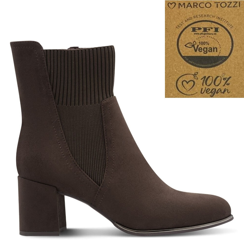 A dark brown suede ankle boot with a ribbed knit side panel and block heel, shown on a white background with a Marco Tozzi vegan certification badge in the top right corner.