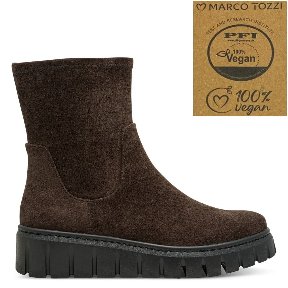 A dark brown suede ankle boot with a chunky black lug sole, shown on a white background with a 'Marco Tozzi 100% Vegan' certification badge in the top right corner.
