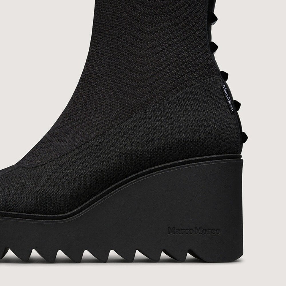 Black stretch wedge boot with studded details on a light grey background