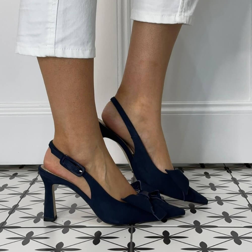 Marian Navy blue high-heeled shoes with bow detail worn by a person on a patterned floor.