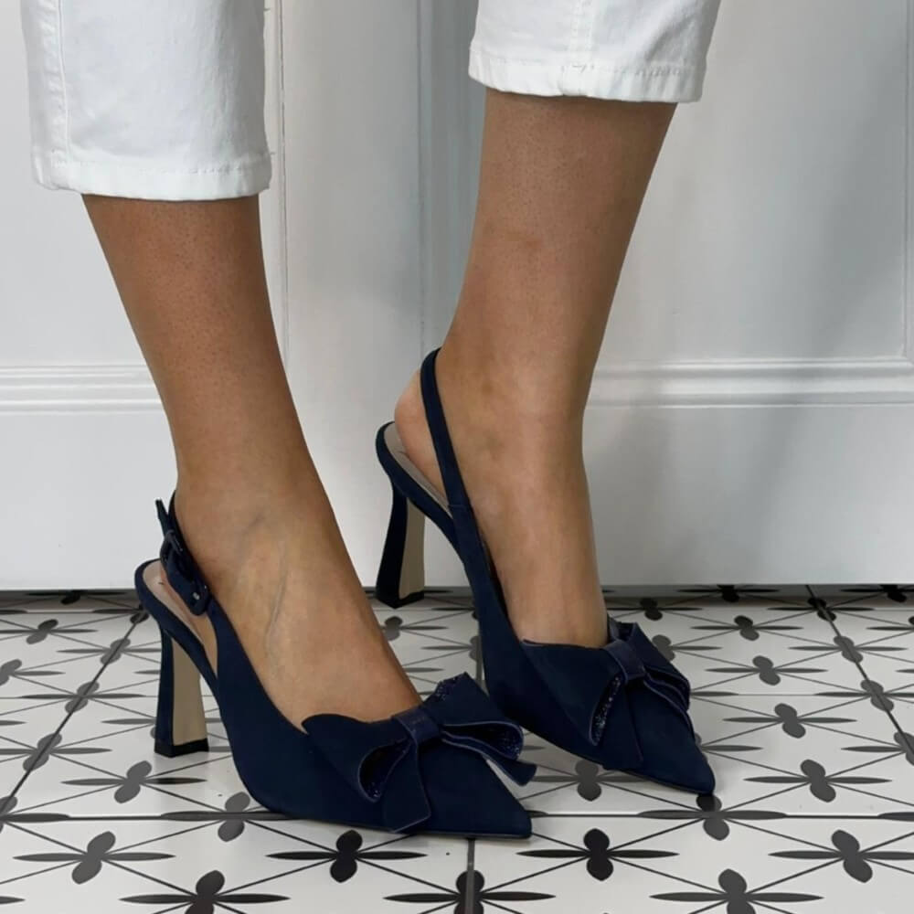 Marian Navy blue high-heeled shoes with bow detail worn by a person on a patterned floor.