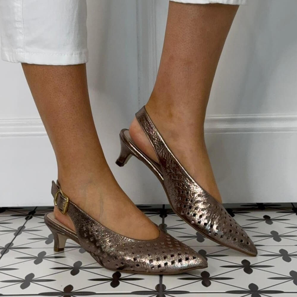 Marian Metallic Bronze Kitten-heeled shoes worn with white pants on a patterned floor.