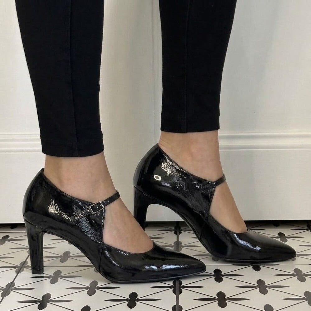 A pair of Marian black patent leather Mary Jane high heels with kitten heels and ankle straps, shown on a model wearing black leggings.