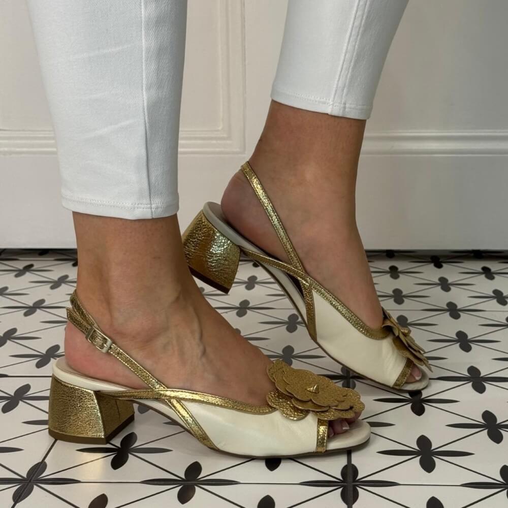 Marian Gold and white sandals with floral details worn on a patterned floor.
