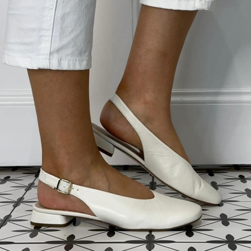 Marian white slingback flats worn with white pants on a patterned floor.