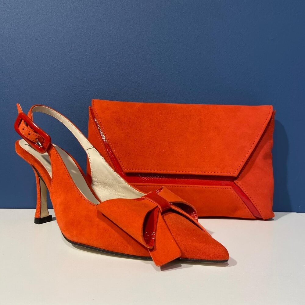 Marian Orange high-heeled shoes with a matching clutch bag on a white surface against a blue background