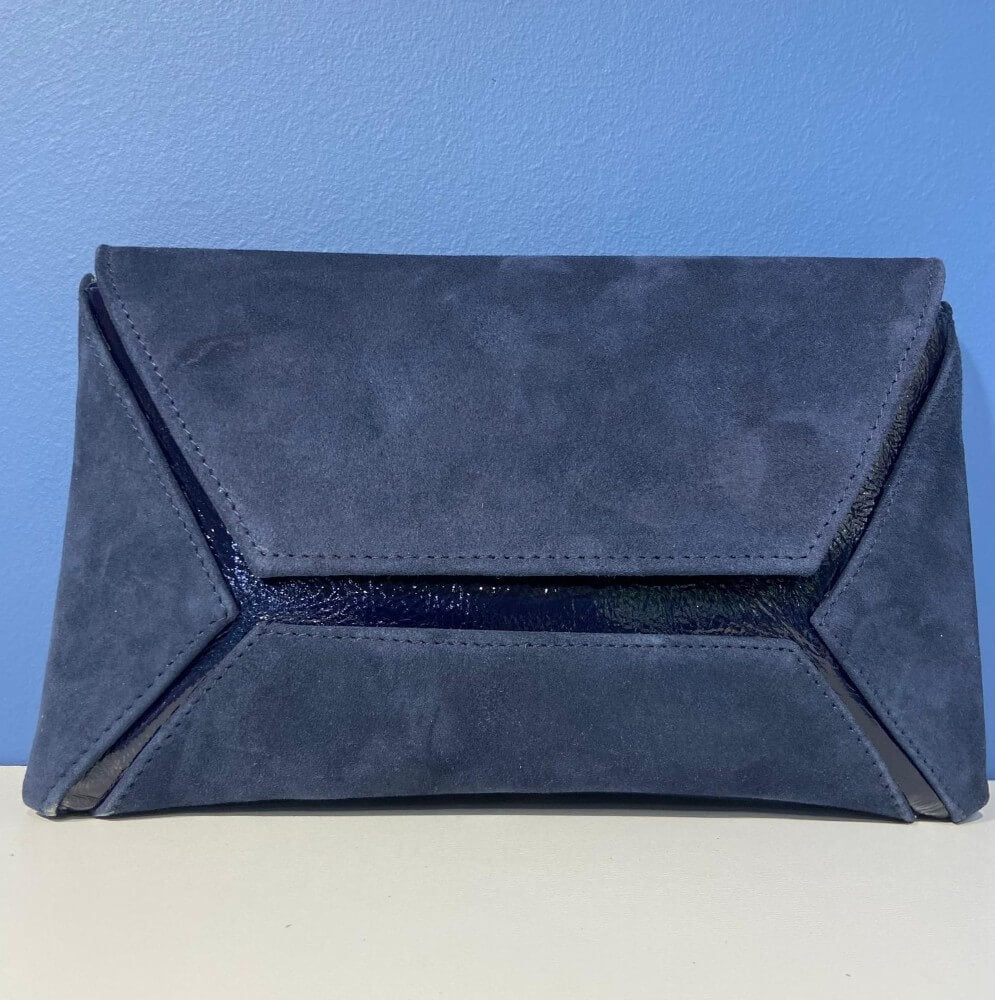 Marian Navy Blue suede clutch bag on a white surface with a blue background