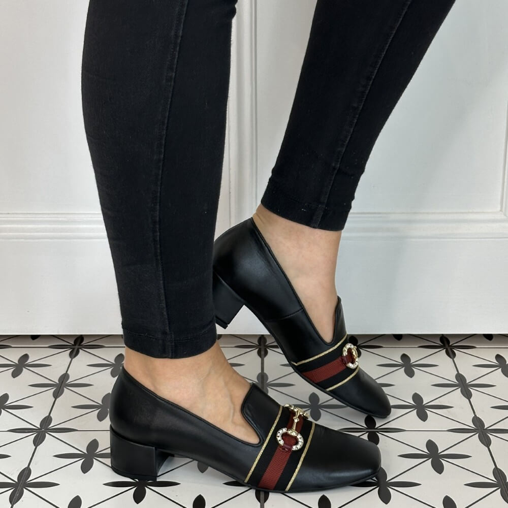 Black leather loafers with red and gold accents worn by a person on a patterned floor.