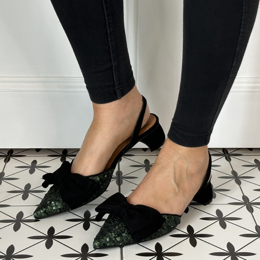 Black pointed-toe shoes with green sequin details worn by a person on a patterned floor.