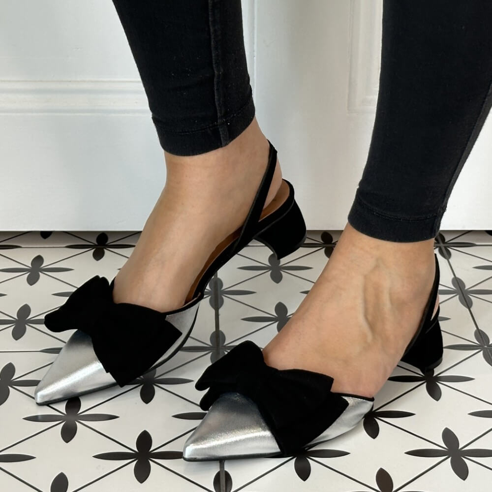 Black pointed-toe shoes with metallic soles worn by a person on a patterned floor.
