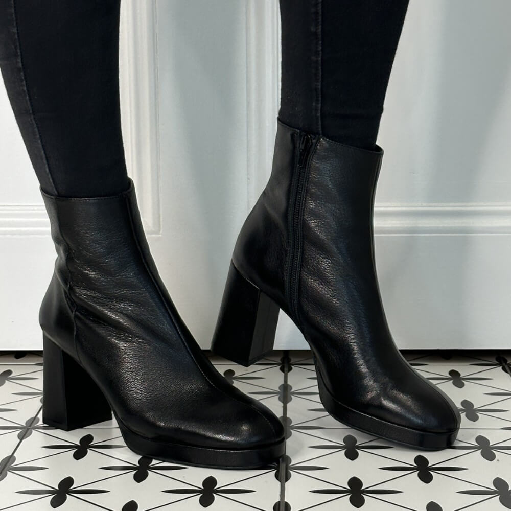 Black leather boots worn with black pants on a patterned floor.