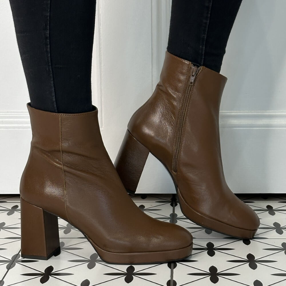 Brown leather platform ankle boots worn with black pants on a patterned floor.