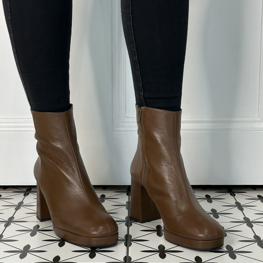 Brown leather platform ankle boots worn with black pants on a patterned floor.