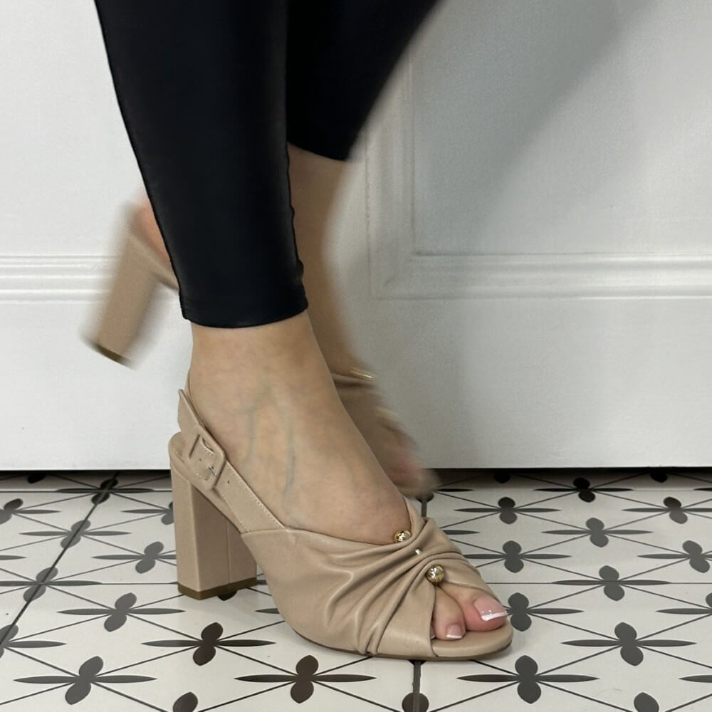Beige high-heeled shoes worn with black pants on a patterned floor.