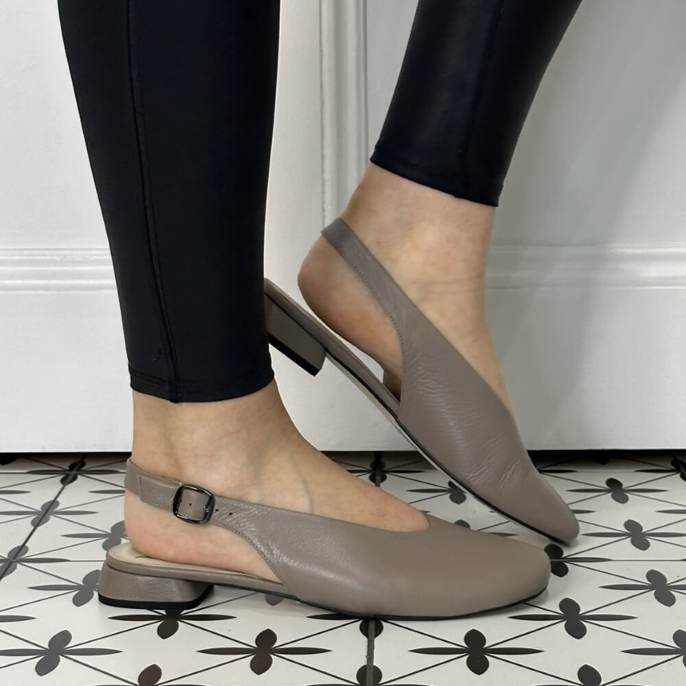 Pair of taupe flats worn with black pants on a patterned floor.