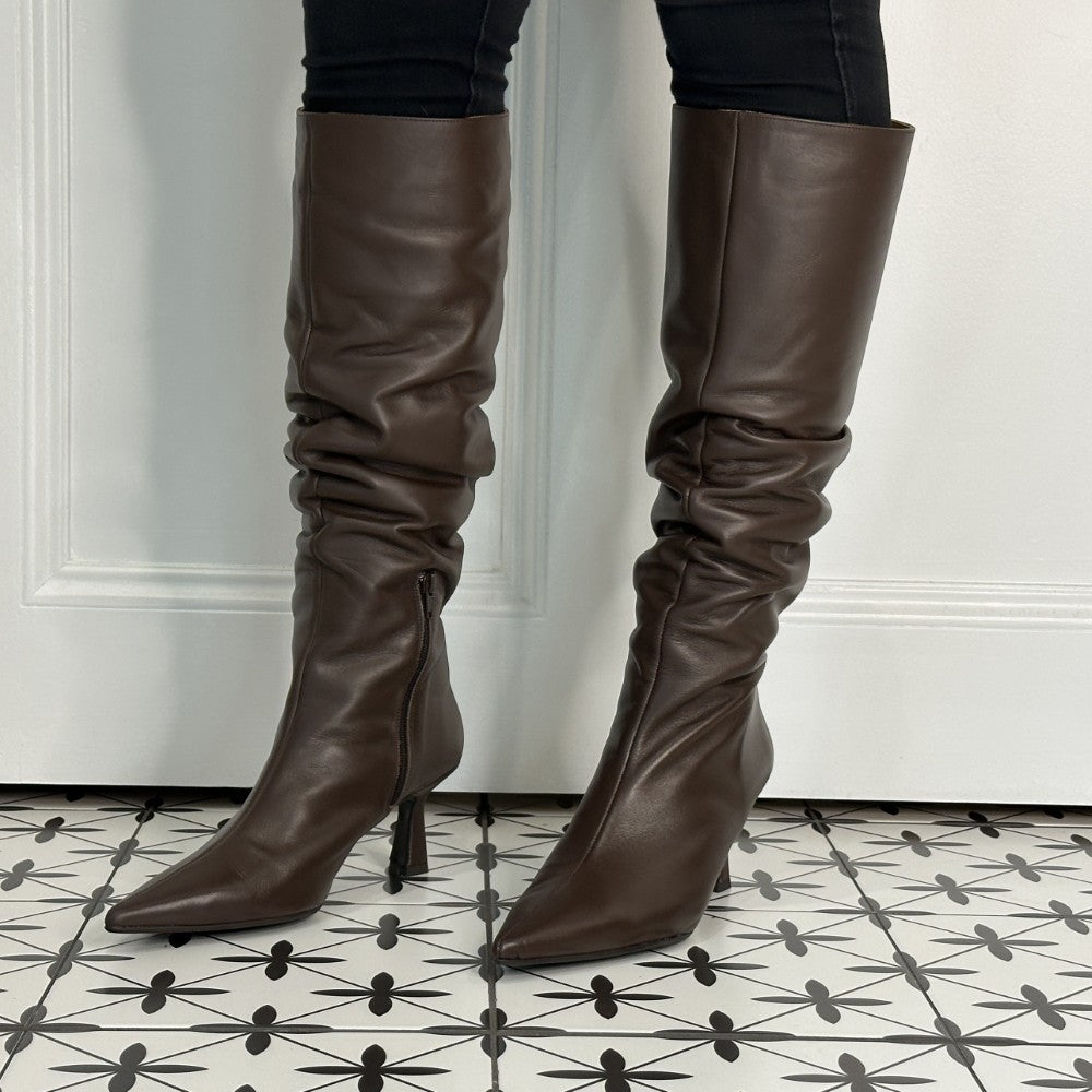 Brown leather knee-high boots with a high heel on a patterned floor.