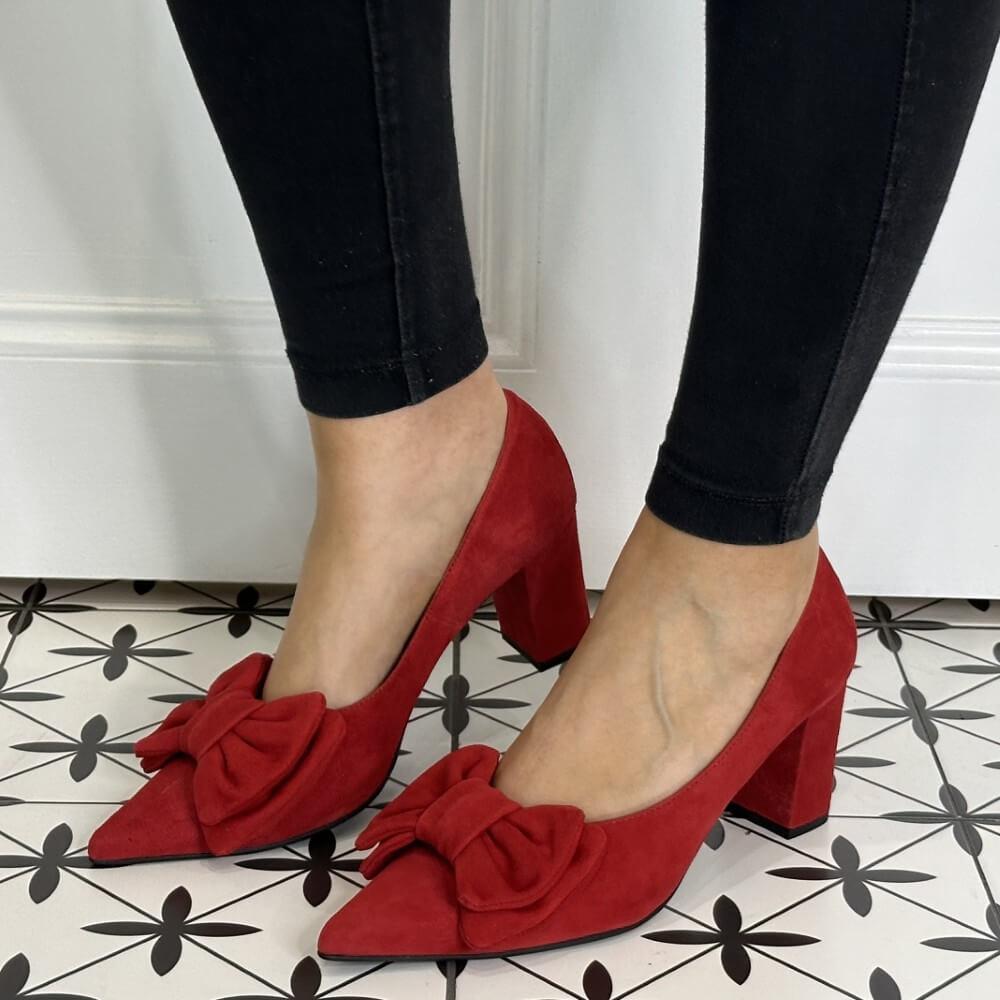 Red high-heeled shoes with bows worn by a person on a patterned floor.