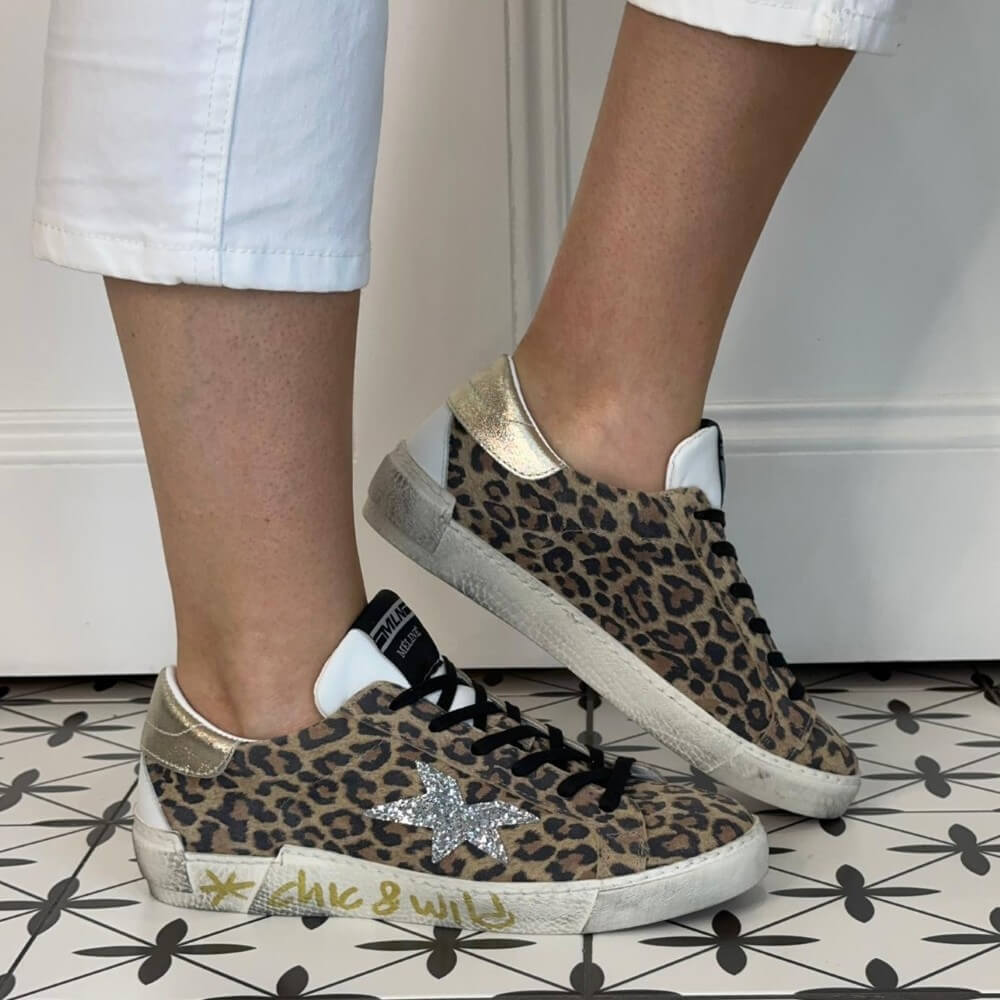 Meline Leopard print sneakers with a star detail worn by a person on a patterned floor.