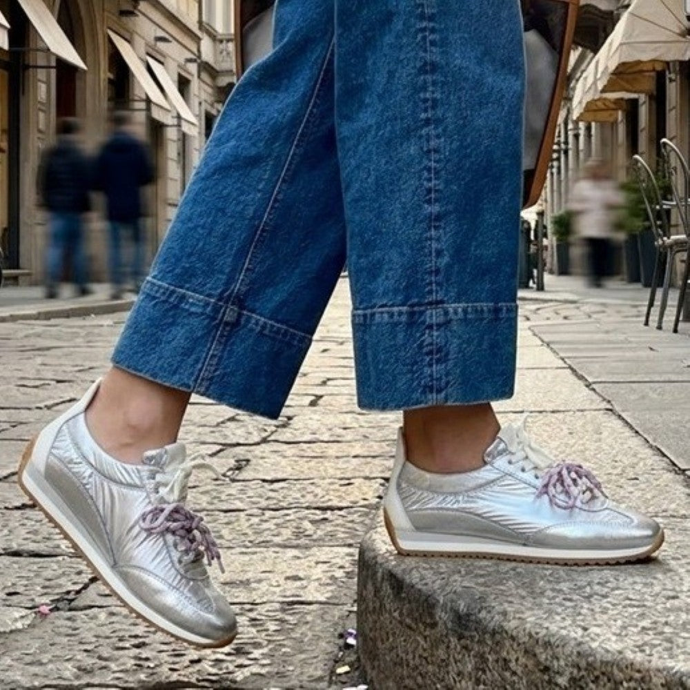 Person wearing Meline silver sneakers with pink laces and blue jeans on a city street.