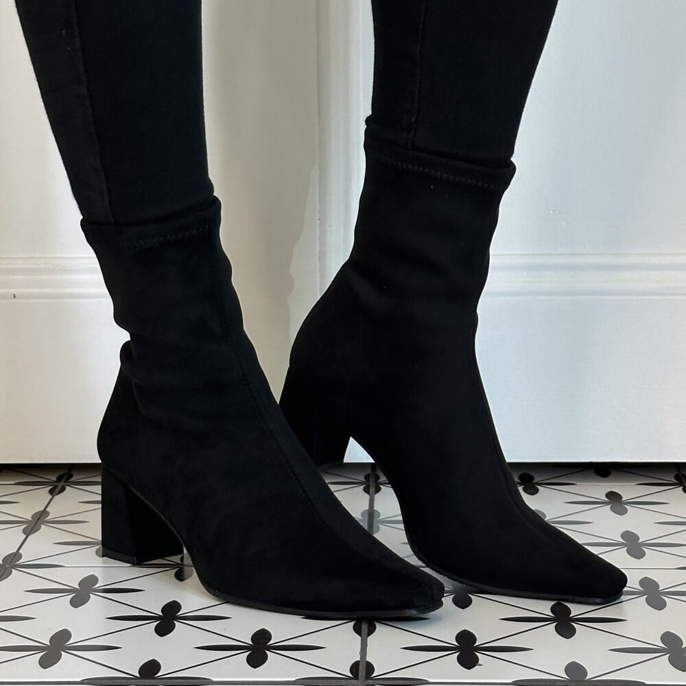 Miss Elastic Black Stretch suede effect ankle boots with block heels and pointed toes, worn with black skinny jeans on a black and white patterned tile floor.