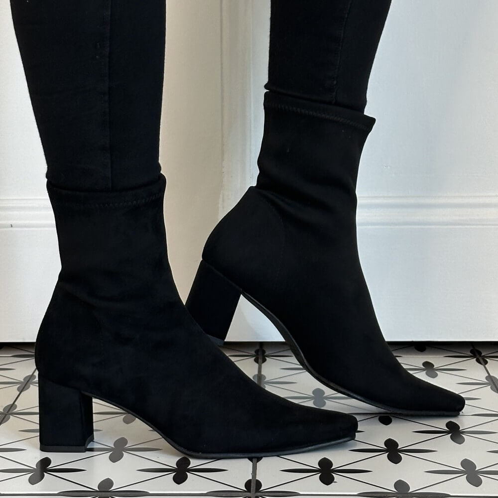 Miss Elastic Black Stretch suede effect ankle boots with block heels and pointed toes, worn with black skinny jeans on a black and white patterned tile floor.