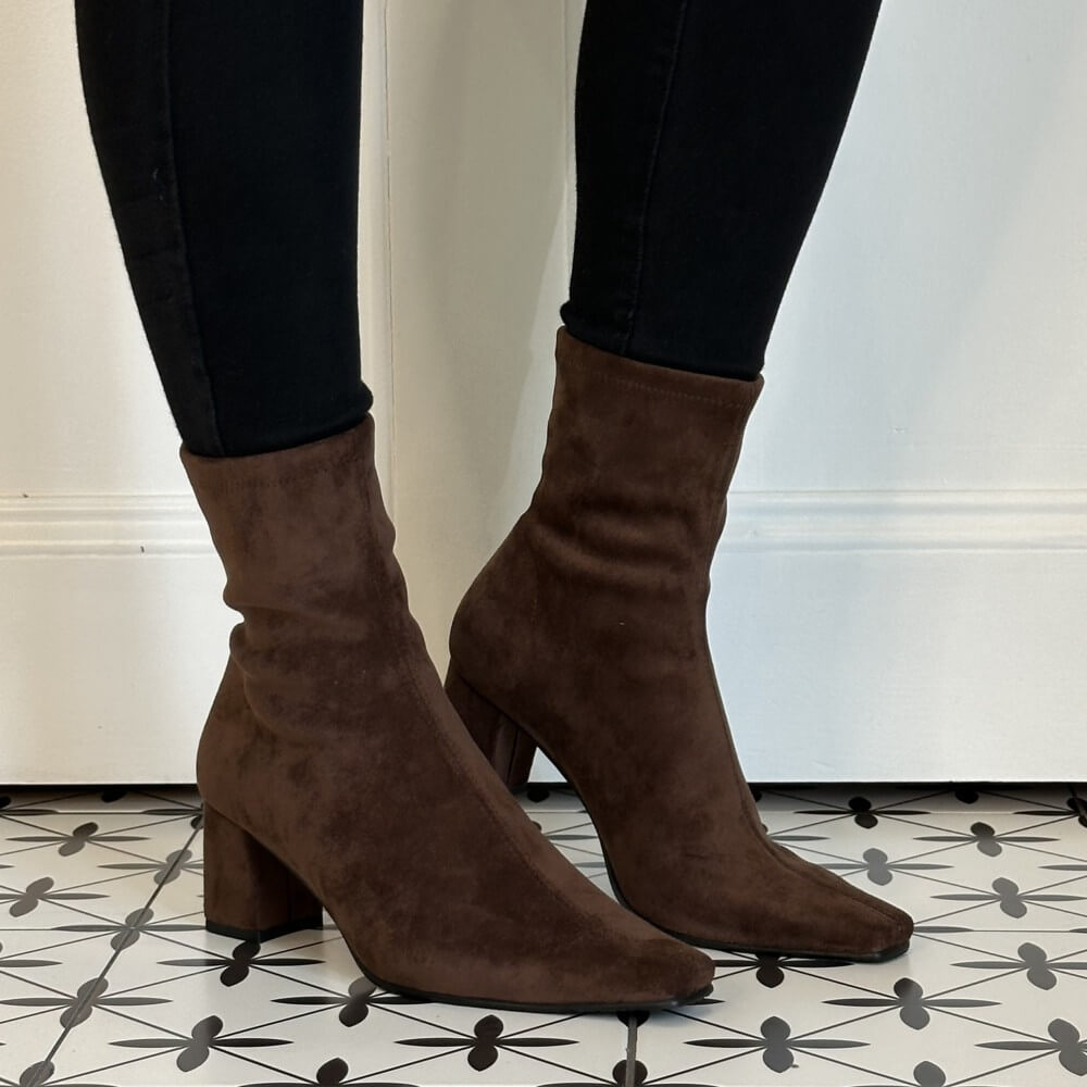 A pair of Miss Elastic dark brown suede ankle boots with block heels and pointed toes, worn with black skinny jeans on a patterned black and white tile floor.