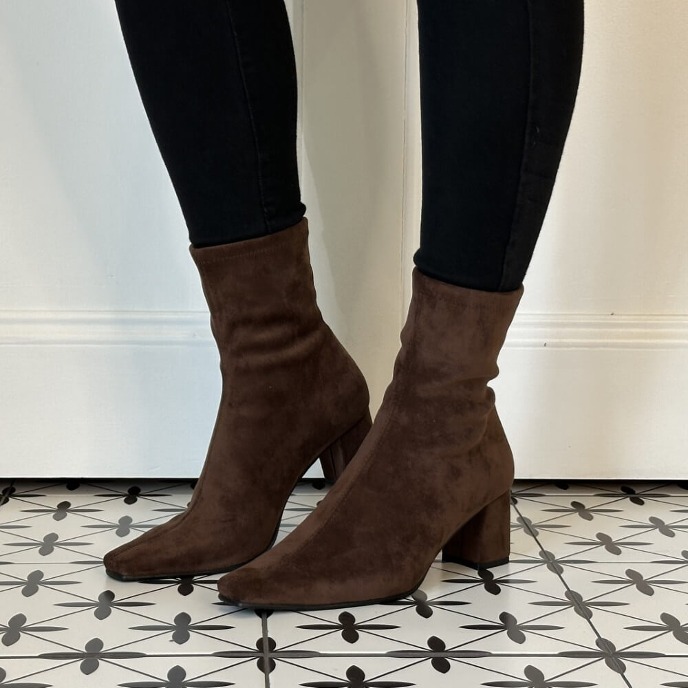 A pair of Miss Elastic dark brown suede ankle boots with block heels and pointed toes, worn with black skinny jeans on a patterned black and white tile floor.