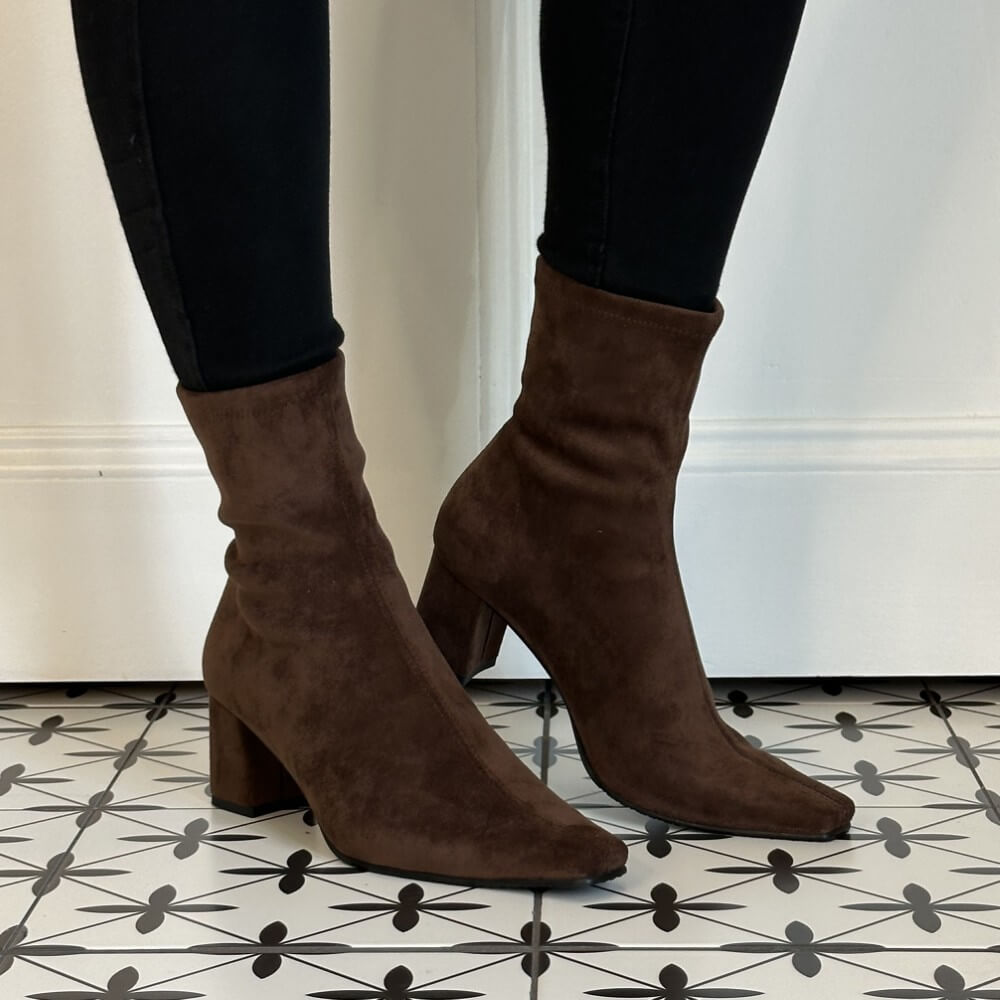 A pair of Miss Elastic dark brown suede ankle boots with block heels and pointed toes, worn with black skinny jeans on a patterned black and white tile floor.