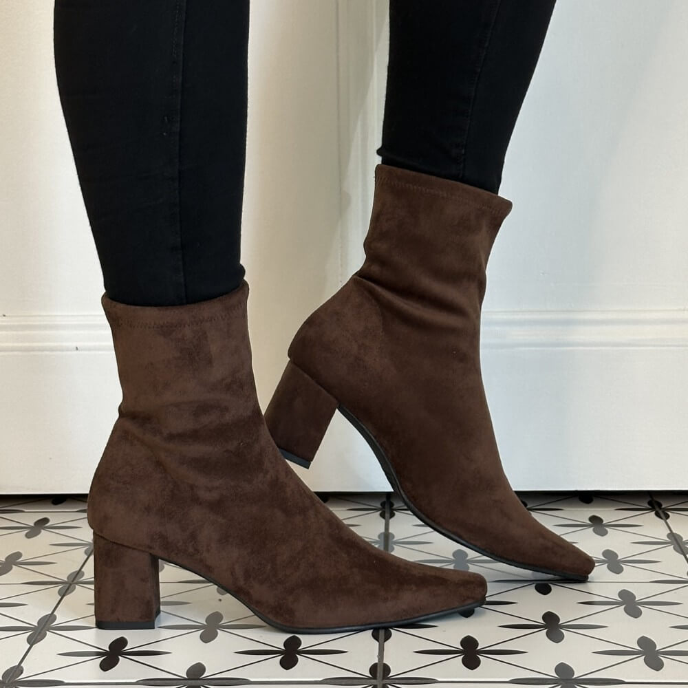 A pair of Miss Elastic dark brown suede ankle boots with block heels and pointed toes, worn with black skinny jeans on a patterned black and white tile floor.