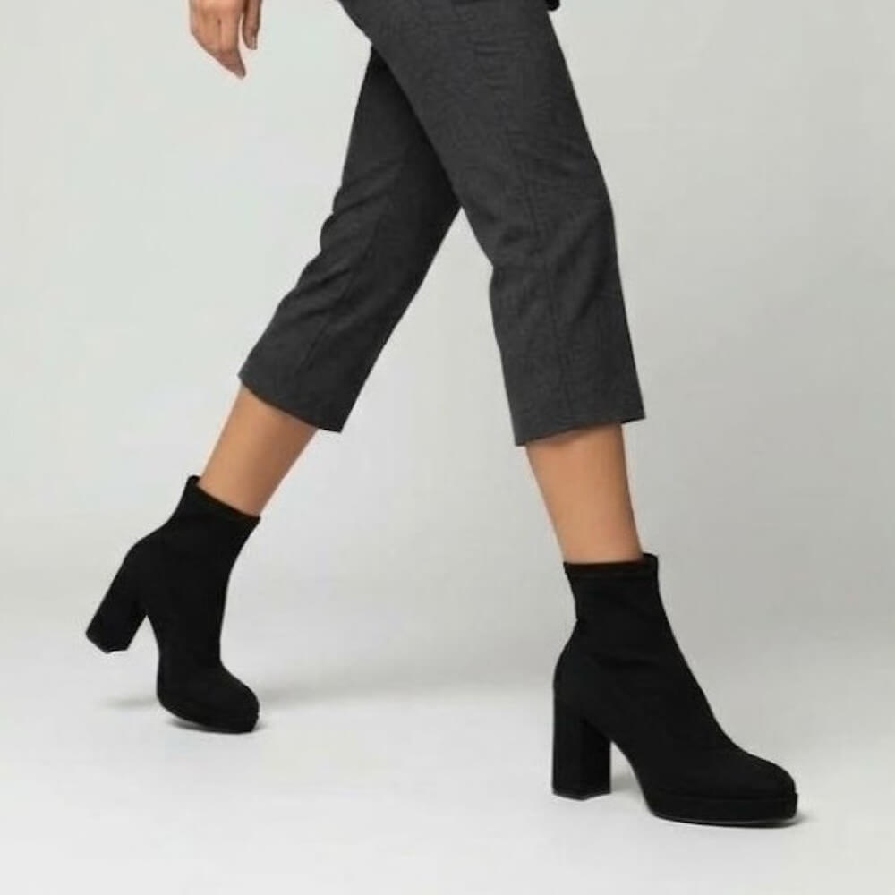 Miss Elastis Black ankle boots with block heels and platform soles, shown on a model wearing dark grey cropped trousers against a light grey studio background.