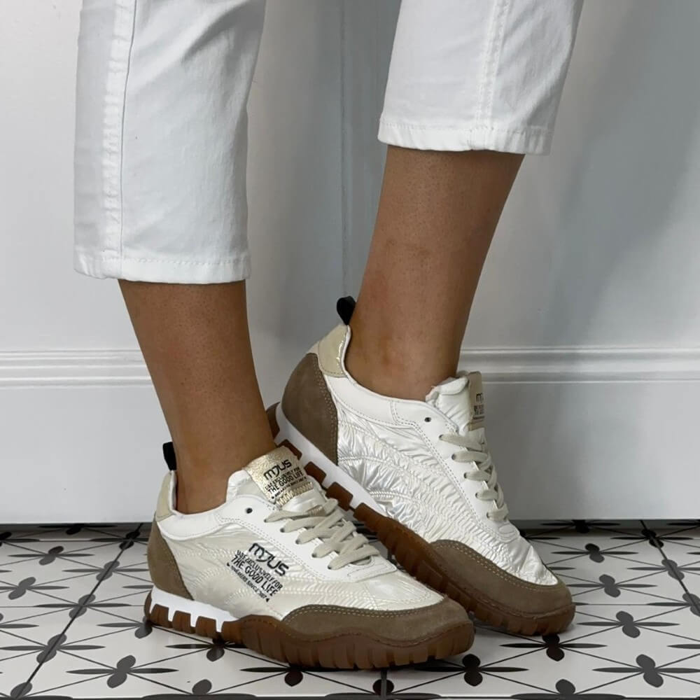 Mjus White sneakers with brown soles worn by a person on a patterned floor.