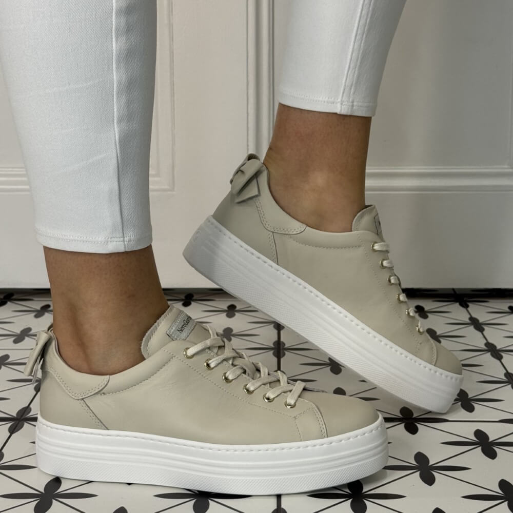 Beige sneakers with white soles worn on a patterned floor. NeroGiardini E506520D-710