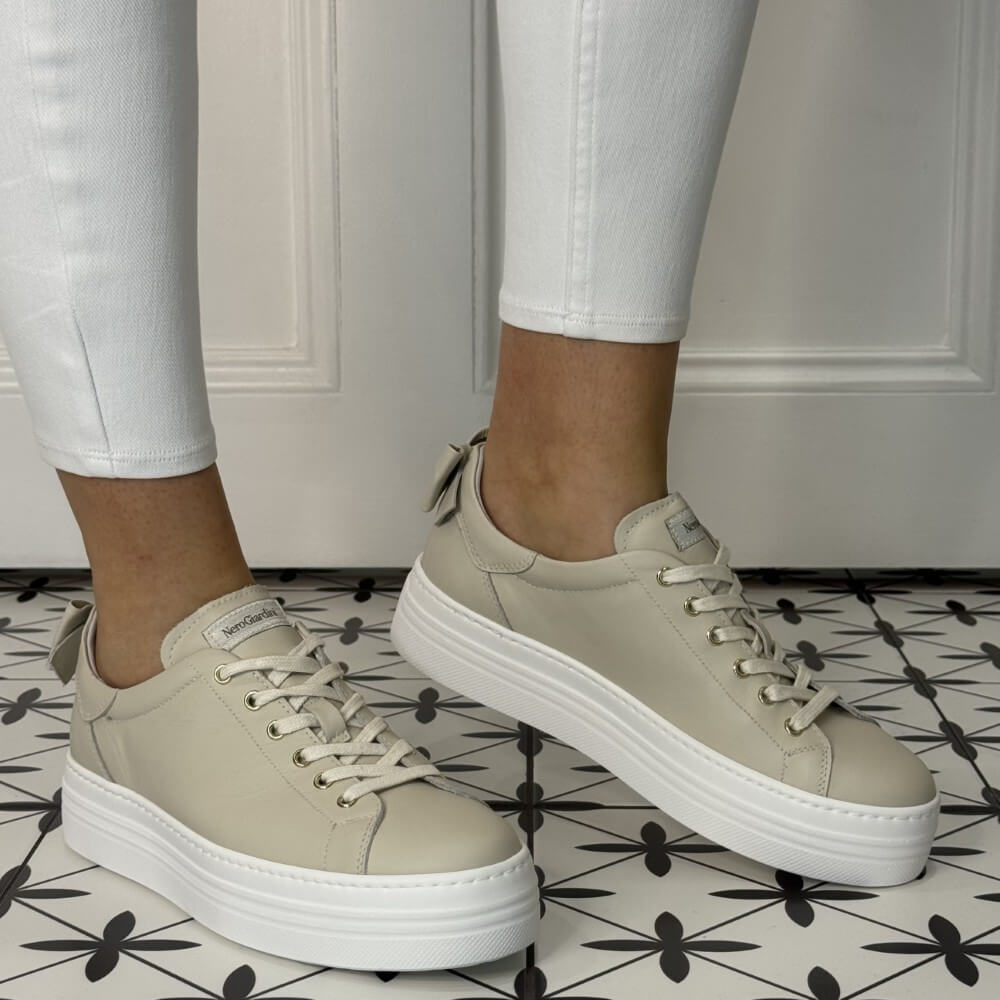 Beige sneakers with white soles worn on a patterned floor. NeroGiardini E506520D-710