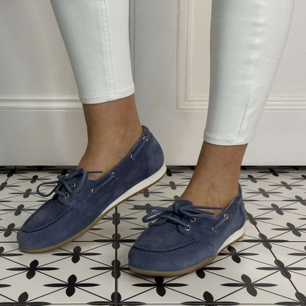 Navy blue loafers worn with white pants on a patterned floor.