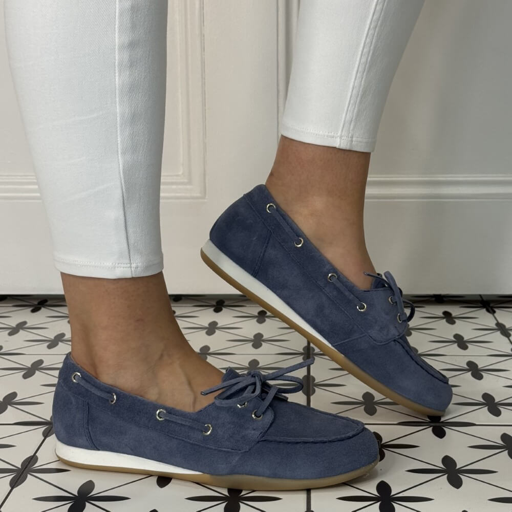 Blue suede boat shoes worn with white pants on a patterned floor.