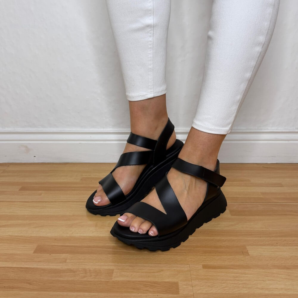 Oh My Sandals 5955 Black sandals worn with white pants on a wooden floor.