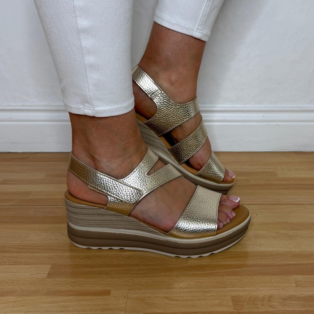 Oh My Sandals 5990 Gold wedge sandals worn with white pants on a wooden floor.