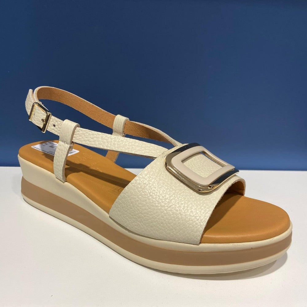 Beige sandal with brown sole on a white surface with blue background